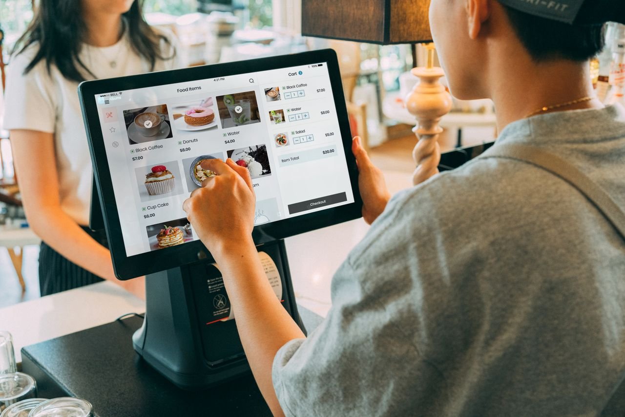 programs-01 A customer using a touch screen system at a cafe counter for modern payment processing.